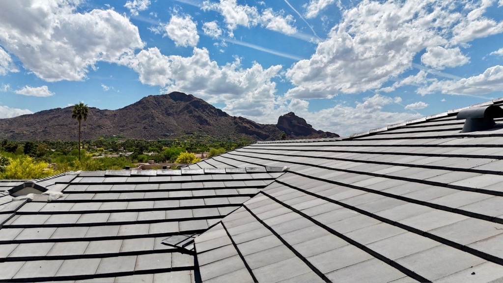 Close-up view of a residential tile roof in Phoenix with Camelback Mountain in the background under a bright, partly cloudy sky.