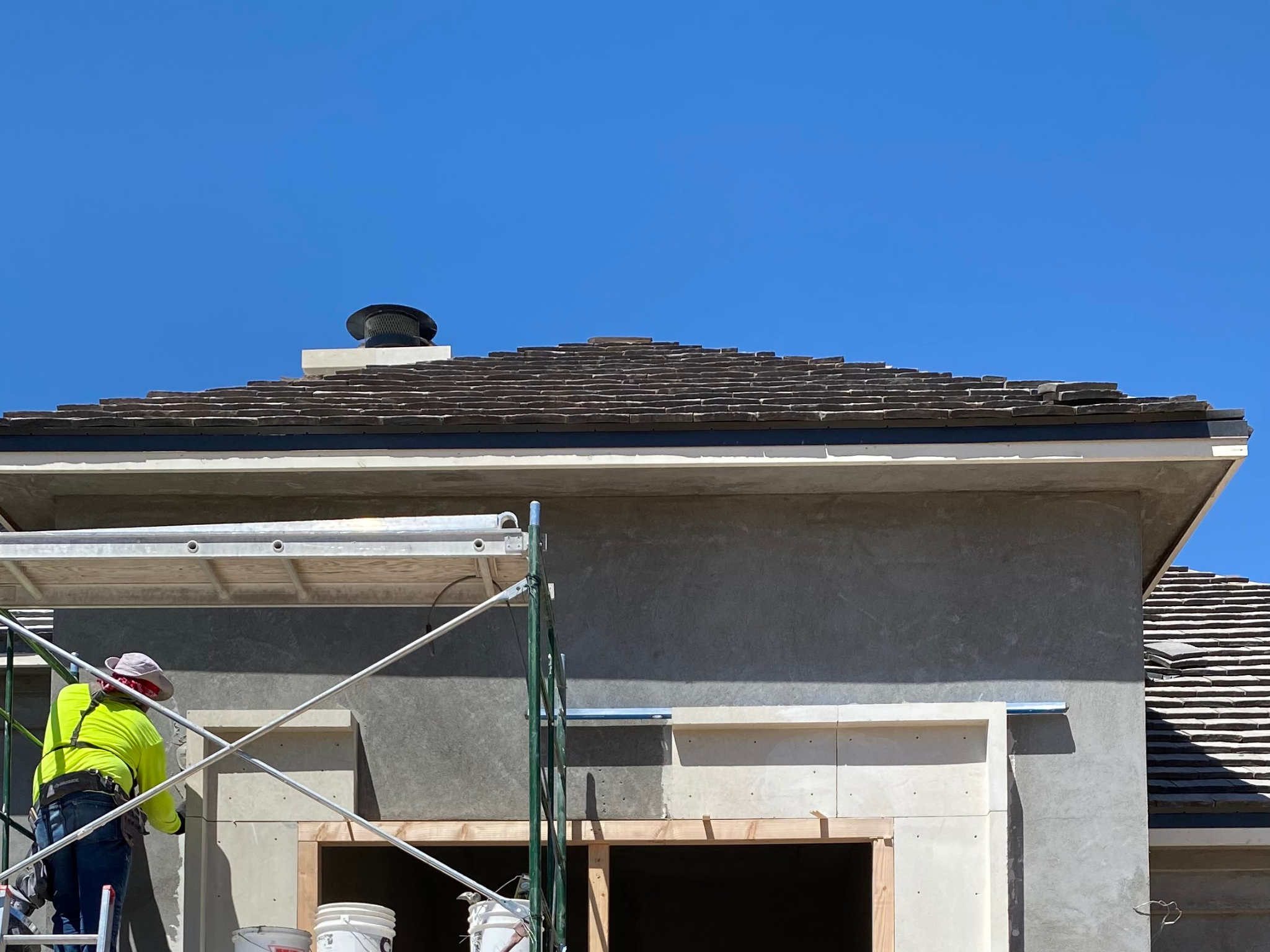 Construction worker applying exterior stucco beneath a newly installed roof on a residential home under renovation in Phoenix, AZ