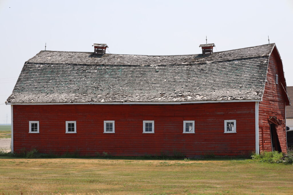 Severely sagging roof on an old red barn, showing structural damage and aging shingles